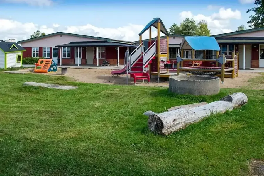 Bild på förskolan med utegård. Förskolan är röd. Utegården har lekställning med rutschkana, sandlåda och grillplats.