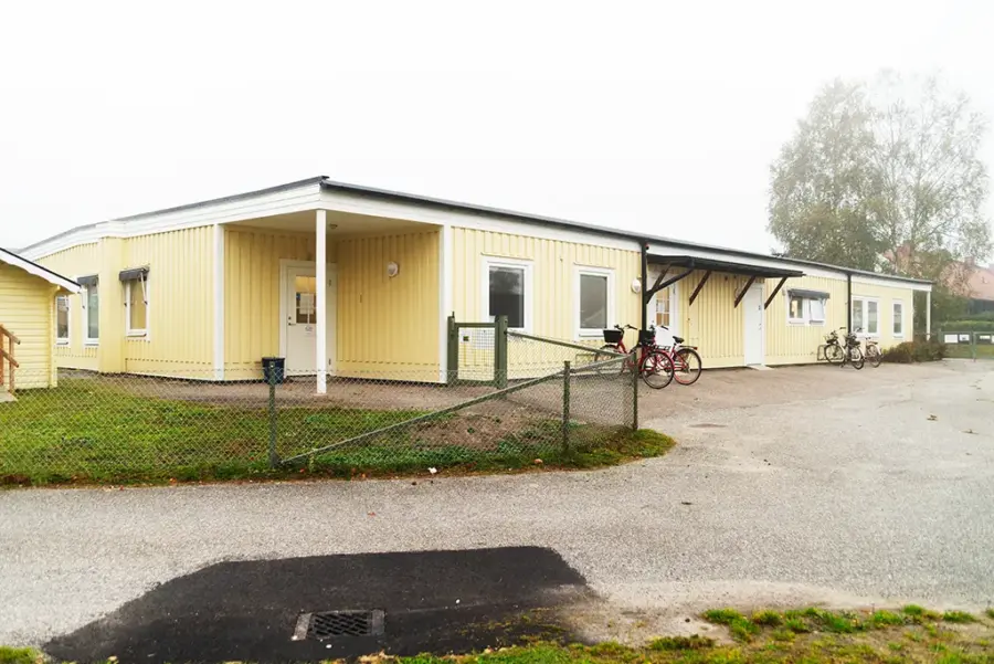 Bild på förskolan utifrån. Byggnaden är gul med vita knutar. På bilden finns cykelparkering och staket.