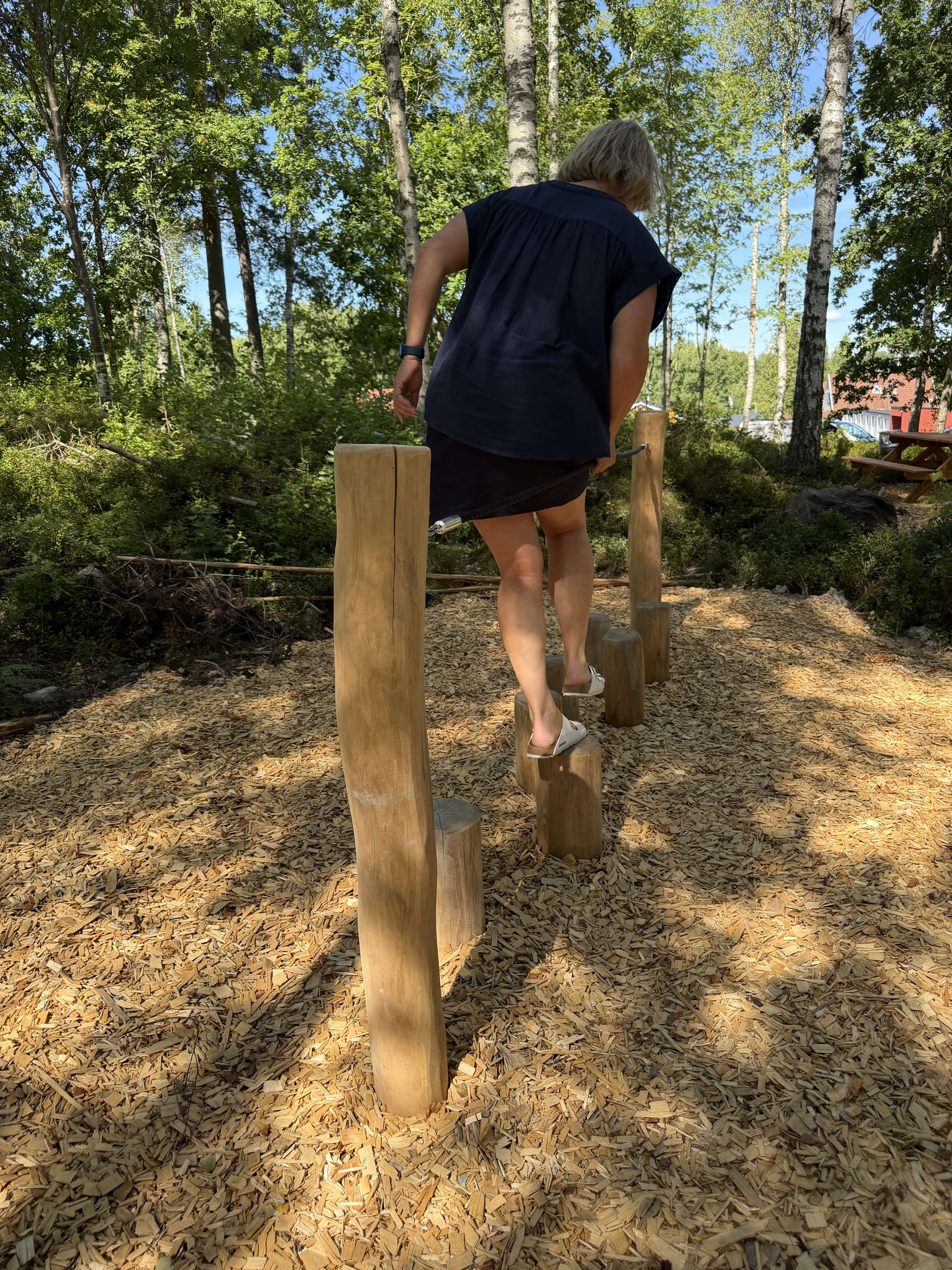En person balanserar på stockar i en lekpark. träd omkring.