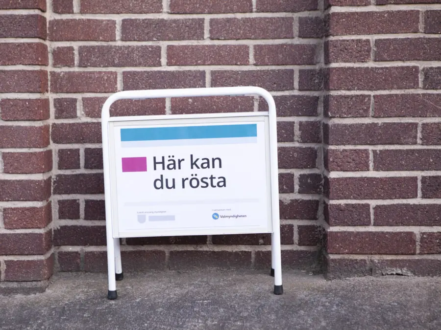 Fotografi av skylt som står mot en tegelvägg, på skylten står det "här kan du rösta"
